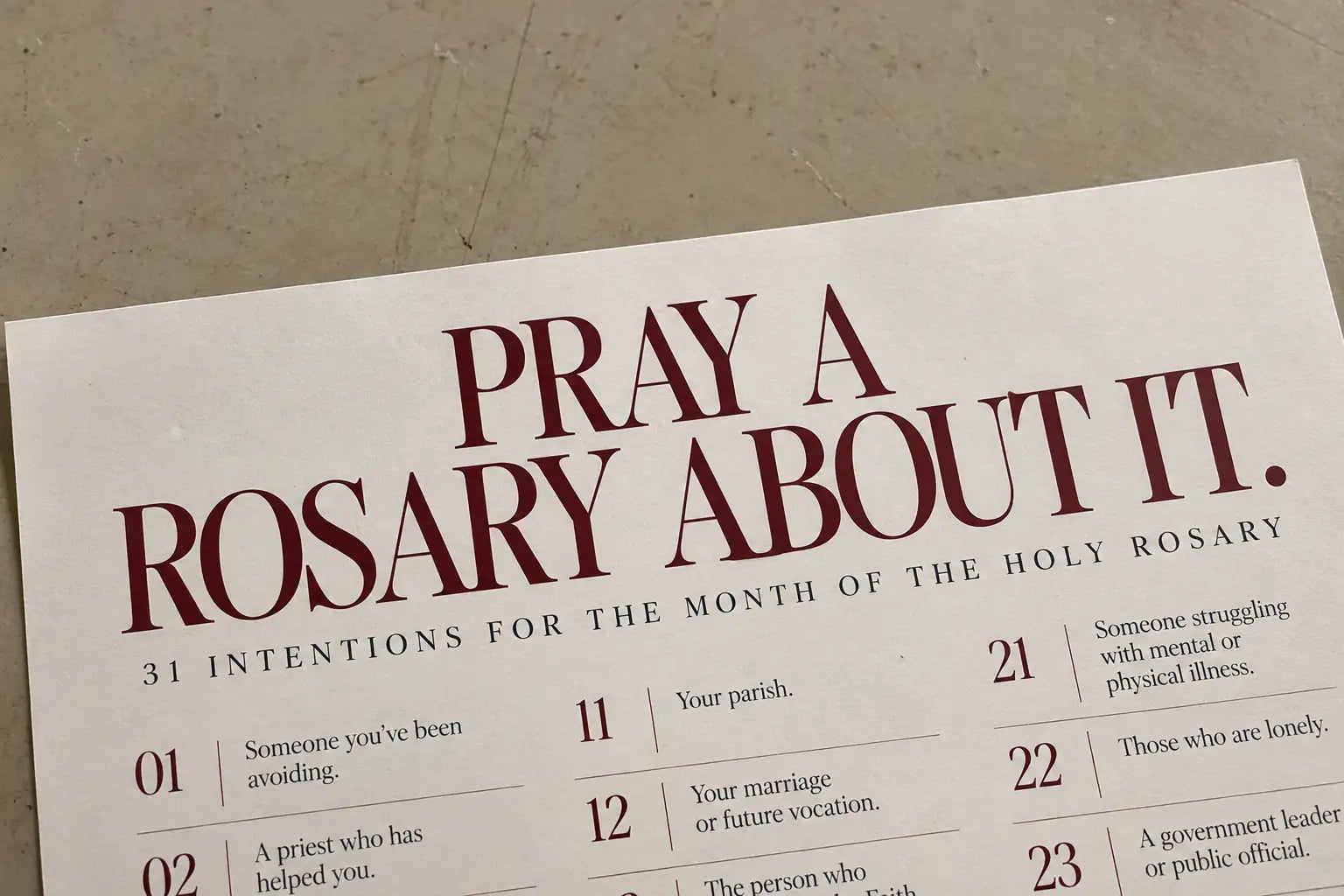 A white paper calendar with maroon text featuring 31 daily prayer intentions for the month of the holy rosary.